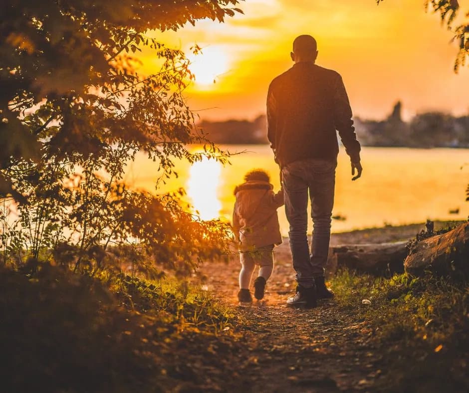 Silhouette of a father and child walking hand in hand at sunset by the water, symbolizing living in the life and godliness God has provided through His love